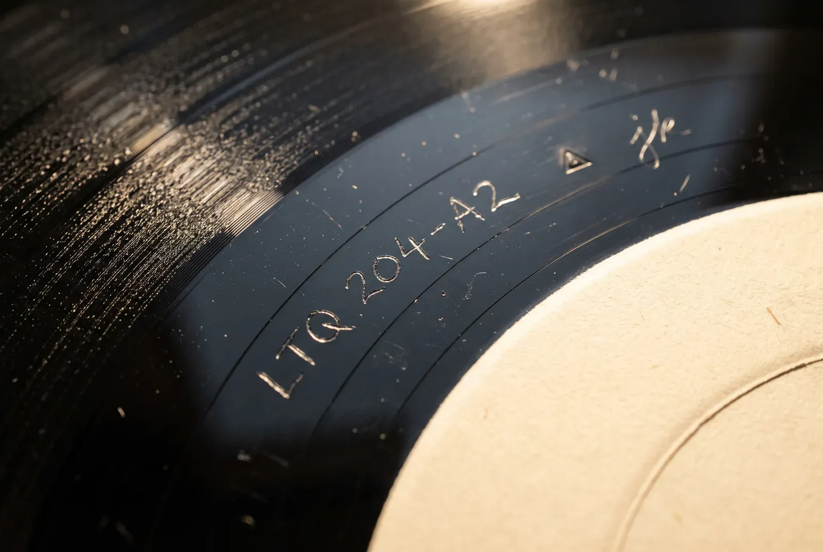 Illustration of the dead wax on side A of the fictional LP Night Ferry Hymns, with LTQ 204-A2 hand-etched, a small stamped triangle and the scratched initials jk beside the cream center label